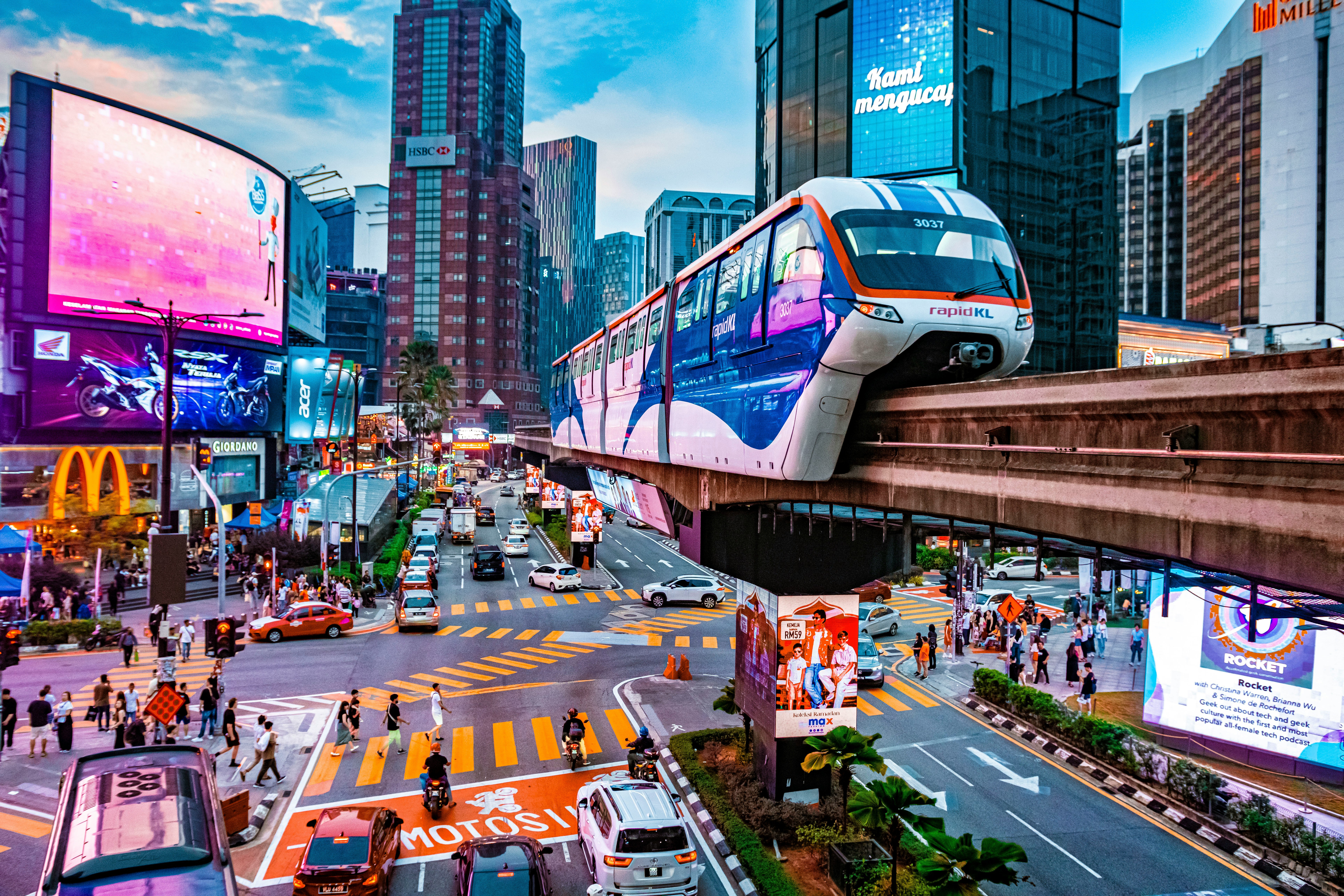 Elevated modern train traveling above a busy city intersection with traffic, pedestrians, and tall buildings in Hong Kong